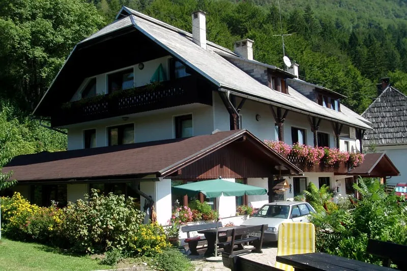 Hiša poleti, z rožami na balkonih, senčnikom in mizami pred vhodom