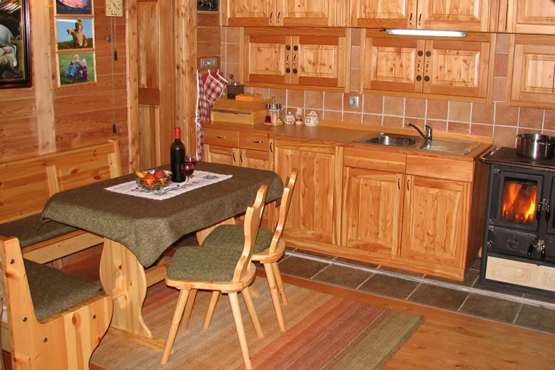 Notranjost koče: lesena kuhinja, miza s klopjo in peč na drva