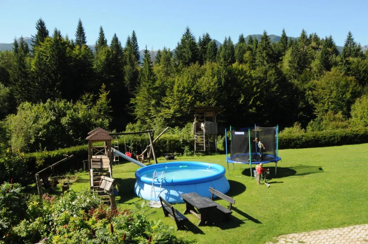Vrt pred hišo z bazenom, trampolinom, igrali in klopmi za piknik